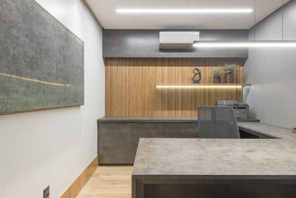 Mesa de trabalho com armários baixos em grafite, painel ripado em madeira e prateleira com iluminação